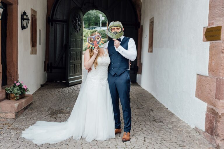 Braut und Bräutigam vor einem alten Torbogen, sie hält den Brautstrauß vors Gesicht