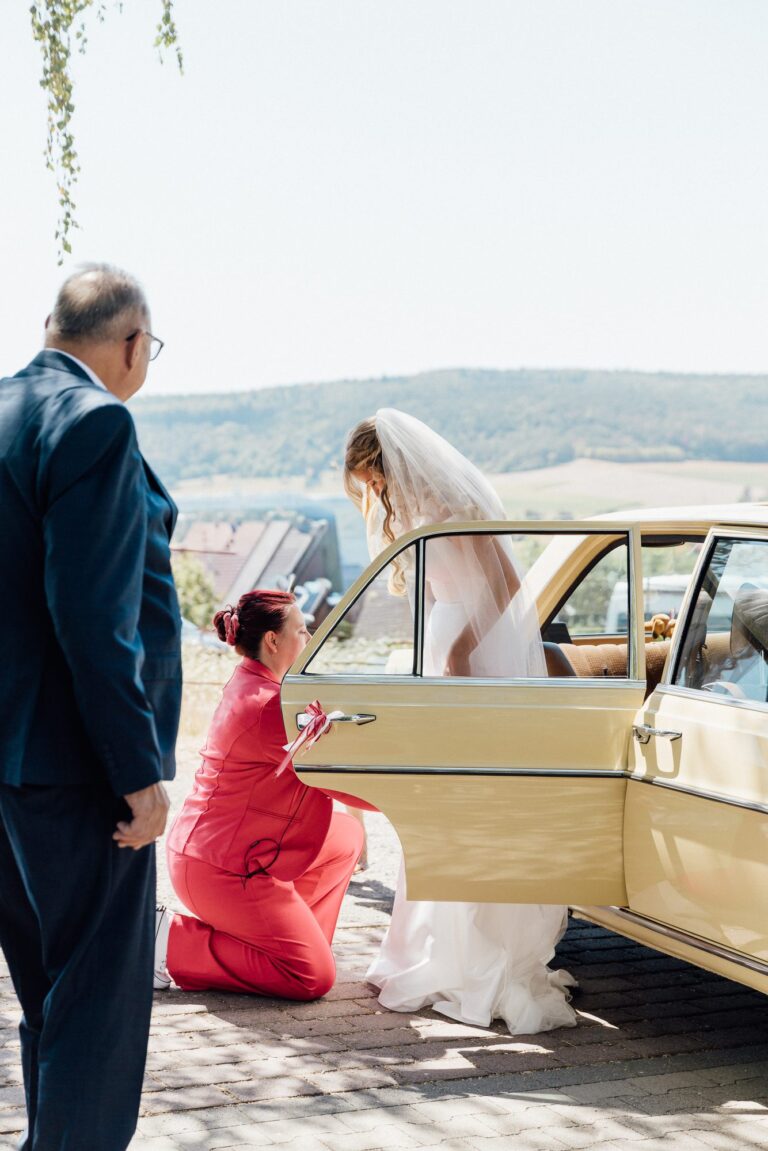 Anna Weber kniet am Auto und richtet Lauras Kleid vor dem Einzug